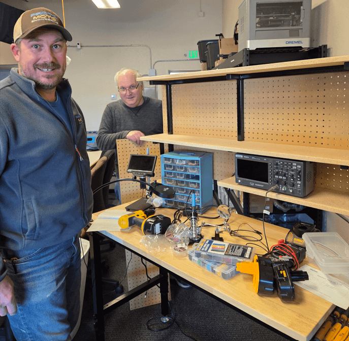 Monumental Impact electronics workbench with soldering tools and oscilloscope.
